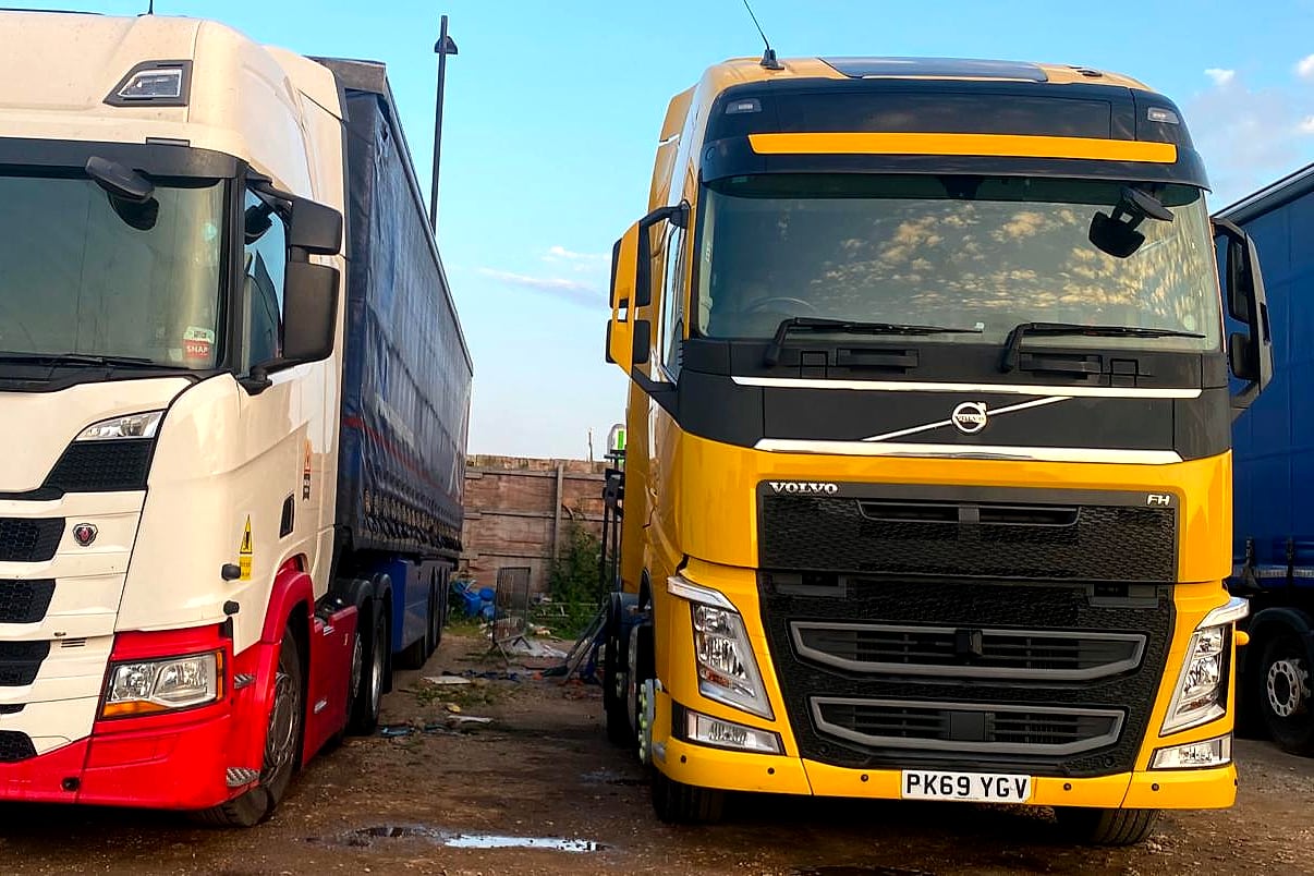 Yellow Volvo FH tractor unit parked front-on beside another unit on the operating centre yard